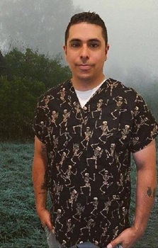 man in spooky landscape wearing a black and grey halloween scrub top with skeletons
