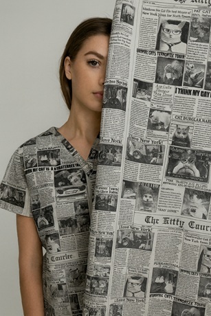 girl wearing cat newspaper print scrub top peeking from behind same fabric